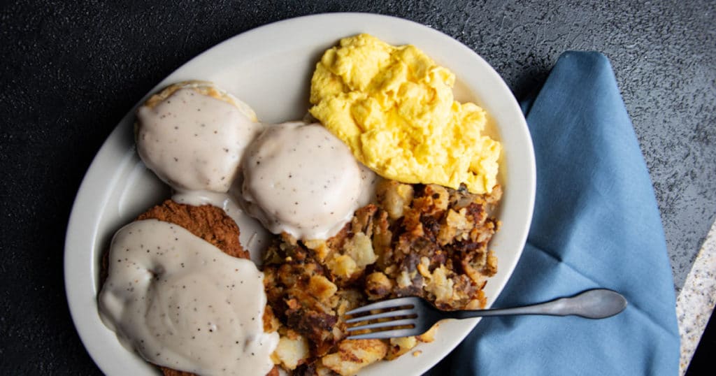 A plate of breakfast from Chompie's with biscuits and gravy, chicken fried steak, potatoes, and eggs