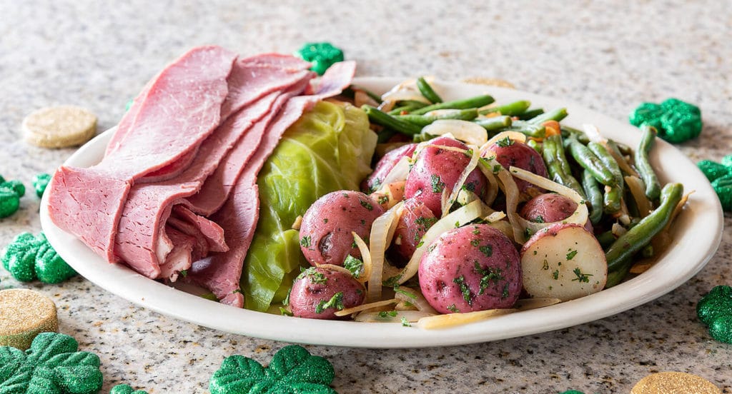A plate of corned beef and cabbage with potatoes and onions on the side