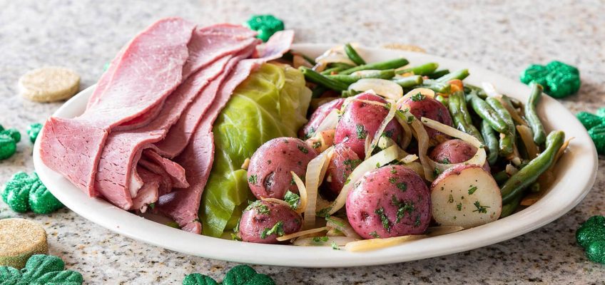 A plate of corned beef and cabbage with potatoes and onions on the side