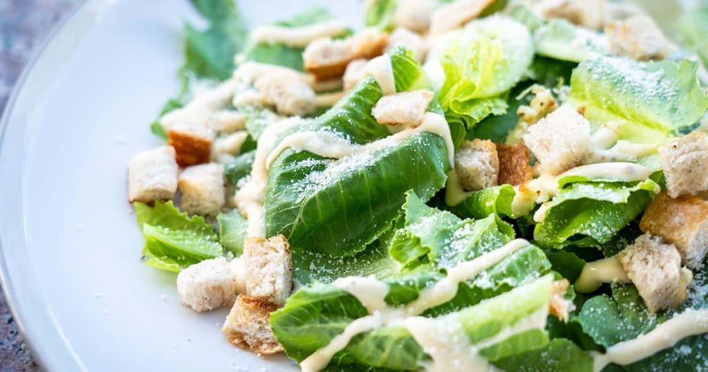 Fresh Caesar Salad on a white plate being served at a restaurant