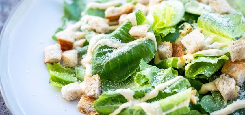 Fresh Caesar Salad on a white plate being served at a restaurant
